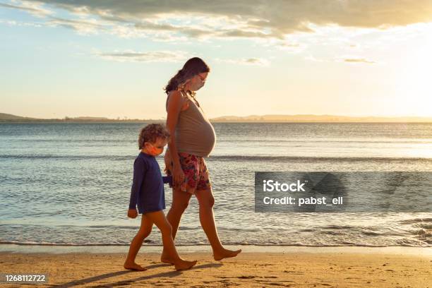 Pregnant Mother Walking Hand In Hand With Son Stock Photo - Download Image Now - Pregnant, Protective Face Mask, Walking