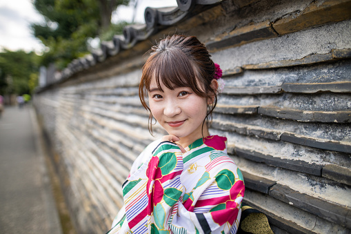 Young woman in yukata leaning on wall and looking at camera