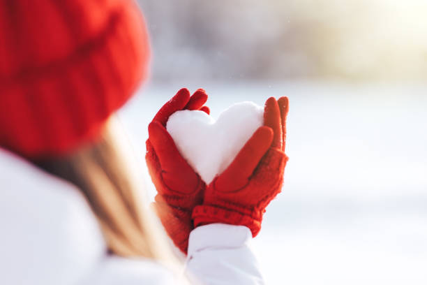 Woman in red gloves and hat holding heart shape from snow stock photo