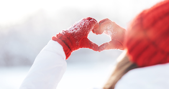 Woman making heart symbol with snowy hands in red gloves, sunny winterday, sun lights, Valentines day, Love concept.