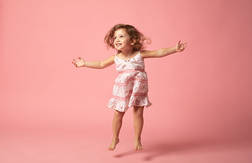 Linda niña con los pies descalzos saltando sobre el fondo rosa. photo