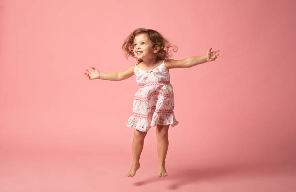 linda niña con los pies descalzos saltando sobre el fondo rosa. - little girls small blond hair child fotografías e imágenes de stock