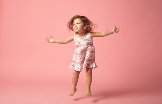 Cute baby girl with barefoot jumping on pink background.