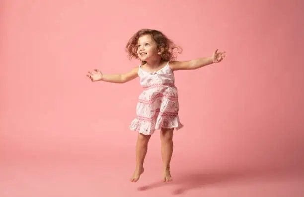 Photo of Cute baby girl with barefoot jumping on pink background.