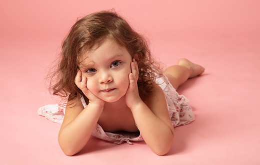Cute little girl lying down on a pink background.