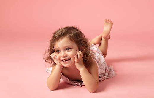 Cute little girl lying down on a pink background.