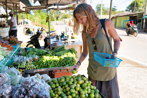 One mid adult Female is buying limes at an outdoor farmers street market located in Ko Lanta, Krabi province, Thailand.