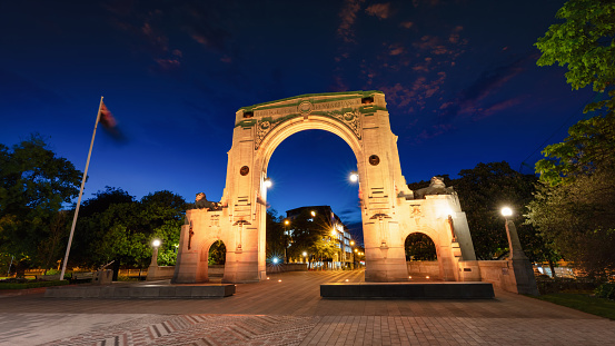 Panorama of the illuminated Arch of Bridge of Remembrance in Christchurch at Night, Sunset Twilight with New Zealand Flag motion blured in the wind. Christchurch, South Island, New Zealand, Oceania