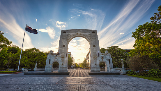 Sunset Panorama of the famous Bridge of Remembrance in Christchurch with New Zealand Flag blowing in the wind. Arch backlit against the sunset Sun. Christchurch, South Island, New Zealand, Oceania