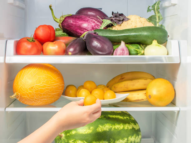 woman takes the plum from the open refrigerator. woman's hand reaches for the vegetables and fruits on the refrigerator shelf. healthy food - plum tomato fotos imagens e fotografias de stock