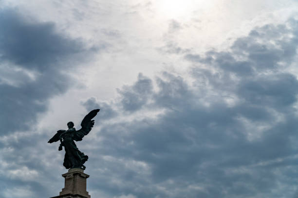istock Statue of an angel in Rome and clouds background with sun rays as divine light 1268159143