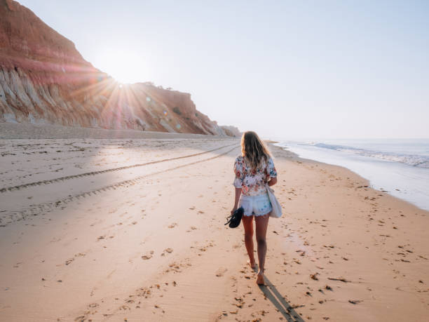Young woman walking on Portuguese beach at sunrise Rear view of woman walking on beach at sunrise albufeira photos stock pictures, royalty-free photos & images