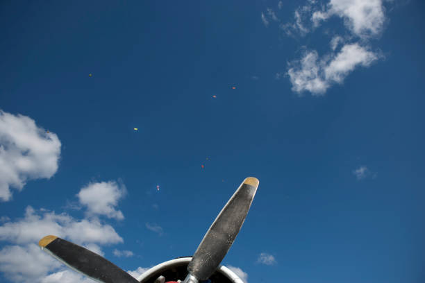 The proppelers of a vintage aircraft and a group of paratroopesr in the blue sky