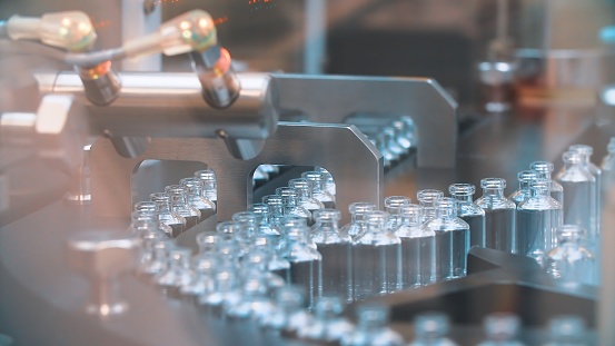 Botellas de vidrio en producción en la bandeja de un dispensador automático de líquidos, una línea para el llenado de medicamentos contra bacterias y virus, antibióticos y vacunas photo