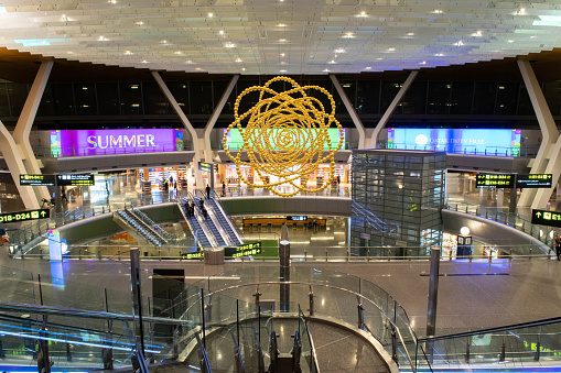 A wide shot of the central atrium connecting Concourses C, D, and E at Hamad International Airport, which features a unique hanging sculpture and roof installation - Doha, Qatar