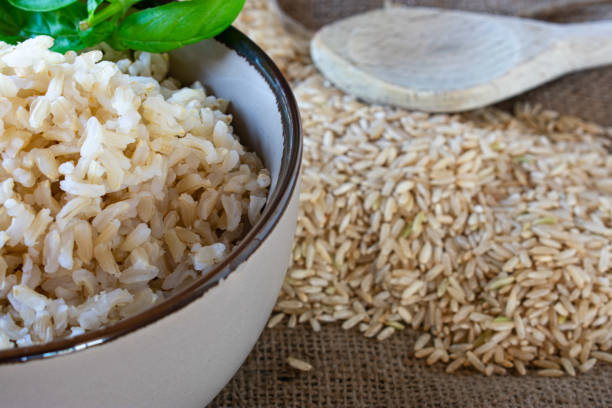 raw and cooked brown basmati rice cooked basmati rice in a beige bowl and raw, dry brown rice on a jute cloth with a wooden spoon basmati rice stock pictures, royalty-free photos & images