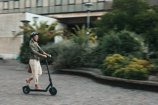 Woman riding an electric scooter to commute to works place. Green incentive promoting the usage of electric scooters.