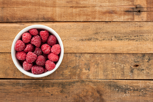 Top view of white bowl full of frozen raspberries over wooden table