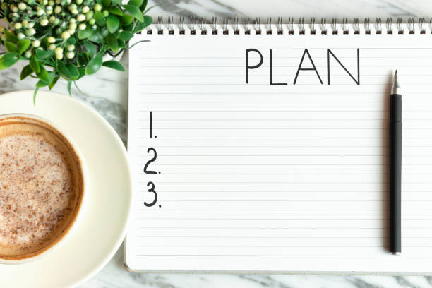 istock Notepad with the inscription plan and cup of coffee on marble background top view. 1268198033