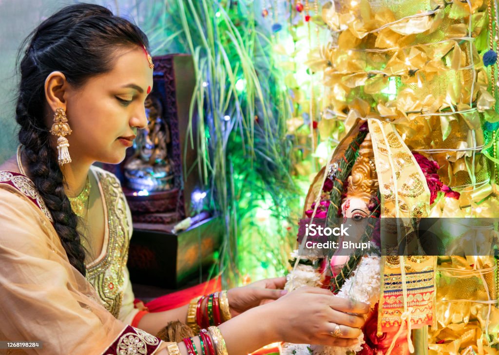 happy Indian young woman celebrating ganesh chaturthi festival. Indoor image of beautiful, happy Indian young woman sitting near ganesha statue and celebrating ganesh chaturthi  festival at home. She is wearing traditional Indian clothes. Ganesh Chaturthi Stock Photo