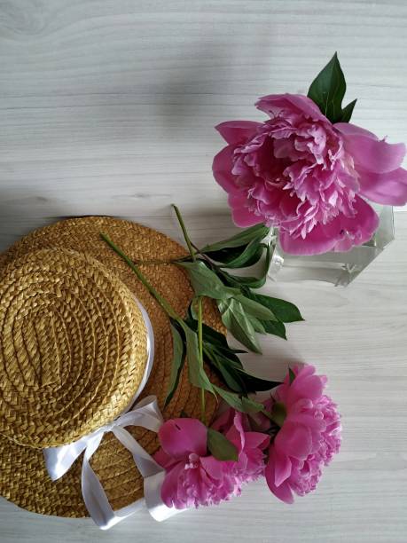 istock Two peonies on a wicker straw hat and one peony standing in a transparent vase 1268198288