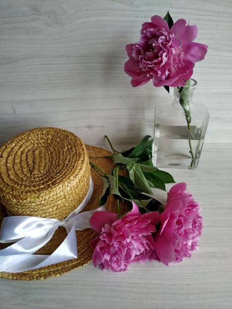 istock Two peonies on a wicker straw hat and one peony standing in a transparent vase 1268198366