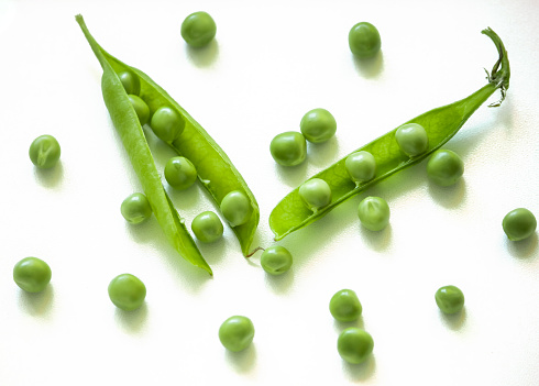 a scattering of peas with green pods on a white background.