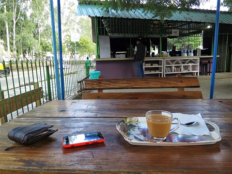 Dimapur, Nagaland, India - November 2014: A glass cup of tea, a phone and wallet on a wooden table in a quiet cafe in the city of Dimapur in Northeast India.