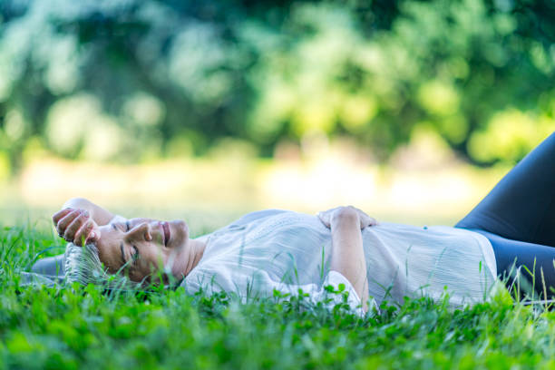 Mindful mature woman meditating by the water, lying down, feeling connected to the earth and nature