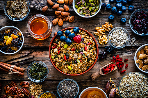 Healthy eating: homemade granola bowl with fruits on rustic wooden table. The composition includes fruits like strawberry, blueberry, dates, honey, raisins, chia seeds, walnut, pumpkin seeds, pistachio. Selective focus on the bowl. Predominant color is brown. High resolution 42Mp studio digital capture taken with Sony A7rII and Sony FE 90mm f2.8 macro G OSS lens