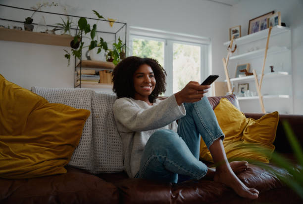 istock Young woman sitting indoor watching tv and holding remote control on sofa 1268220083