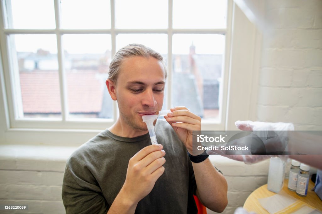 Collecting Saliva Close-up of an unrecognisable mature caucasian health professional wearing gloves handing a young male a test tube for him to collect his saliva in. Saliva - Bodily Fluid Stock Photo