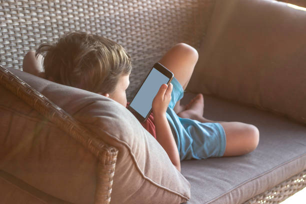 istock Adorable little boy relaxing on couch and holding mobile in hands. 1268220320