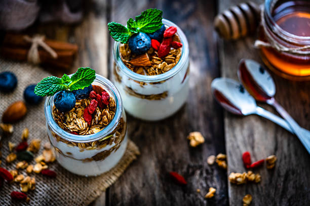 Healthy eating: high angle view of two glass containers with yogurt, granola and berries shot on rustic wooden table. Selective focus on top of the bowls. High resolution 42Mp studio digital capture taken with Sony A7rII and Sony FE 90mm f2.8 macro G OSS lens