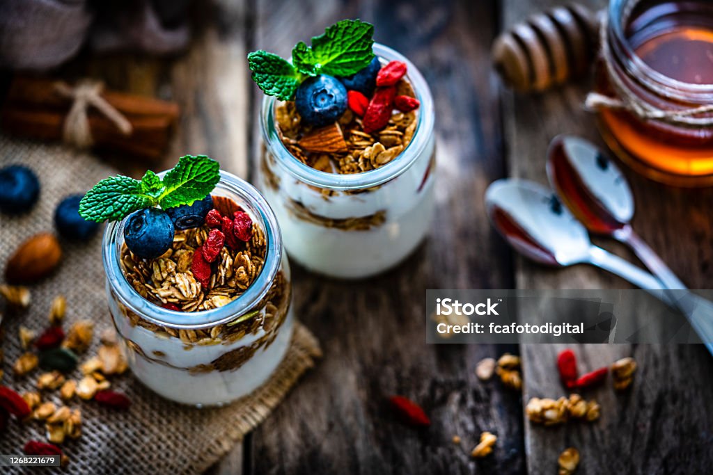 Healthy eating: yogurt with granola and berries Healthy eating: high angle view of two glass containers with yogurt, granola and berries shot on rustic wooden table. Selective focus on top of the bowls. High resolution 42Mp studio digital capture taken with Sony A7rII and Sony FE 90mm f2.8 macro G OSS lens Yogurt Stock Photo