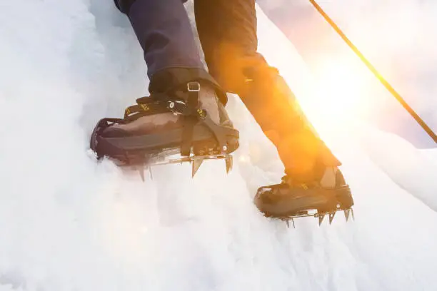 Close up of climber climbing ice mountain in mountainering shoes with strong lens flare