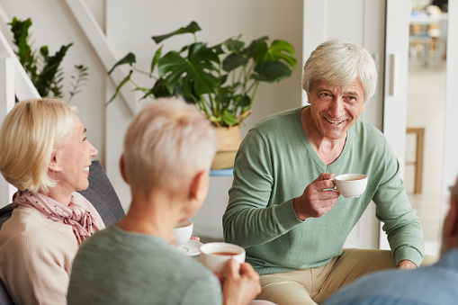 Group of senior friends gathering together to drink tea and talking to each other at home