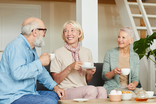 Group of happy senior people smiling to each other and drinking tea at home