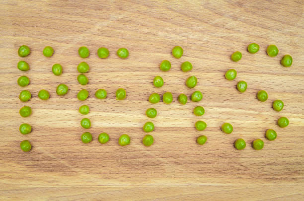 word pea is written in green pea seeds on a wooden background close up