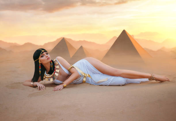 egypte style femme de luxe riche. sexy belle déesse fille reine cléopâtre se trouve sur les pyramides jaunes de désert de sable. art ancien pharaon costume blanc robe or accessoires noir perruque égyptienne maquillage - cleopatra pharaoh ancient egyptian culture women photos et images de collection