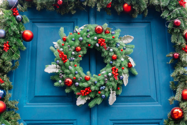 Christmas decor of the front door. Christmas wreath of fir branches on a blue wooden door and a garland of fir branches. blue house red door stock pictures, royalty-free photos & images