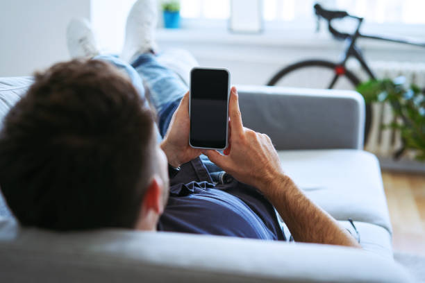 istock Close-up of man holding smartphone while lying on the couch at home 1268237995