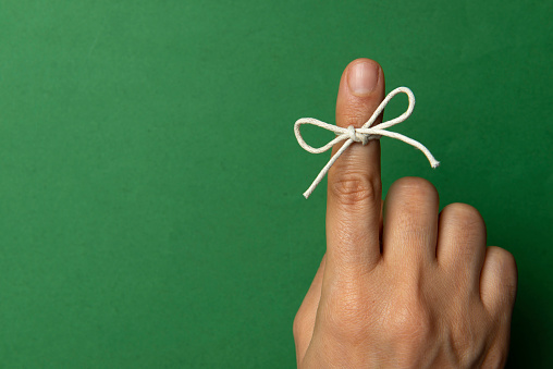 Hand and string tied on index finger on green background.