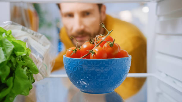 istock Camera Inside Kitchen Fridge: Handsome Man Opens Fridge Door, Thinks to take Bowl of Tomatoes. Man Preparing Healthy Meal. Point of View POV Shot from Refrigerator full of Healthy Food 1268244682