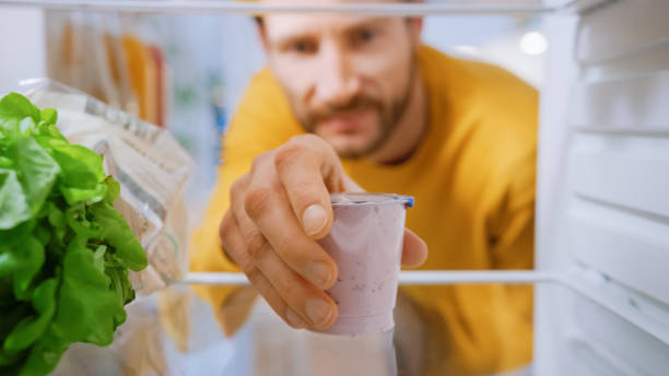 kamera in der küche kühlschrank: handsome man öffnet kühlschrank tür, nimmt joghurt. mann essen gesund. standpunkt pov schuss aus dem kühlschrank voller gesunder lebensmittel - beautiful smiling vegetable calcium stock-fotos und bilder