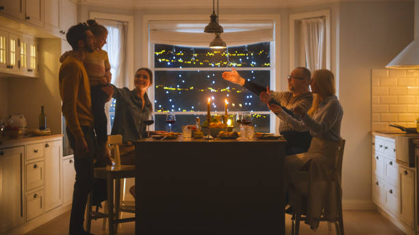 一緒に祝う幸せな家族は、おいしい夕食の食事を食べるテーブルに座っています。小さな子供,若い夫,妻,祖父と祖母,物語を語る,冗談を言う, 楽しい, 喜びであること - grandmother senior adult family domestic kitchen ストックフォトと画像