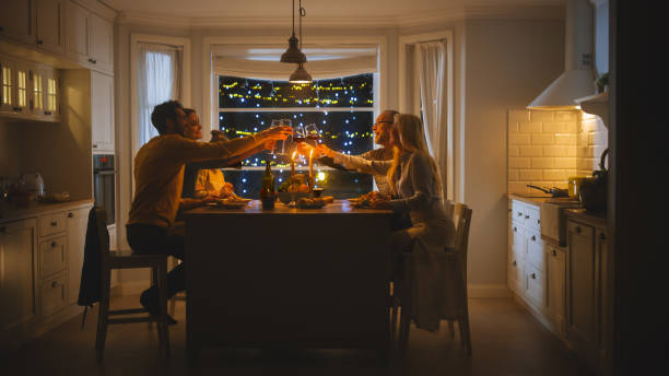 glückliche familie feiert zusammen, sitzen am tisch essen köstliche abendessen. kleines kind, junger ehemann, frau, großvater und großmutter, geschichten erzählen, scherzen, gläser zum toast heben - grandparent grandfather granddaughter little girls stock-fotos und bilder