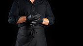 chef in black shirt and apron puts black latex gloves on his hands before preparing food