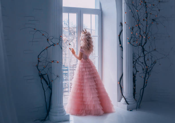 Fairy tale woman princess turned away enjoy view from window. Beautiful carnival pink air tulle, lush full gown. Blond long wavy hair royal crown back, rear view. white antique columns black tree room Fairy tale woman princess turned away enjoy view from window. Beautiful carnival pink air tulle lush full gown. Blond long wavy hair royal crown back, rear view. white antique columns black tree room dark pink dress stock pictures, royalty-free photos & images
