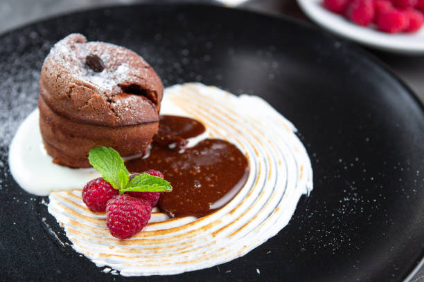 istock Chocolate pudding lava cake with vanilla cream, raspberry and mint on a black plate. Sweet muffins for dessert 1268258166